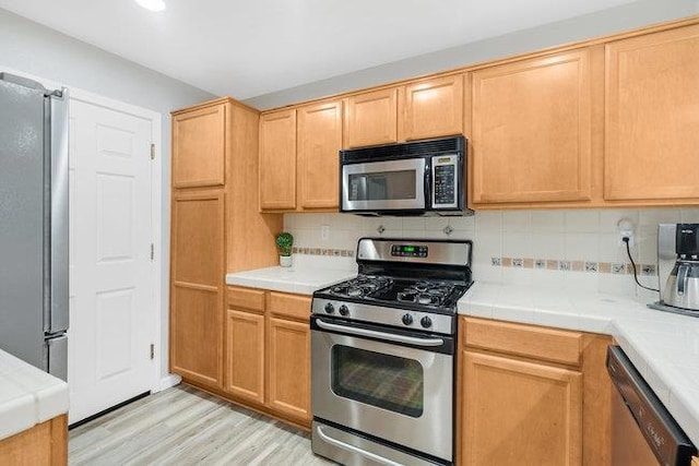 kitchen featuring tasteful backsplash, appliances with stainless steel finishes, tile counters, and light hardwood / wood-style floors