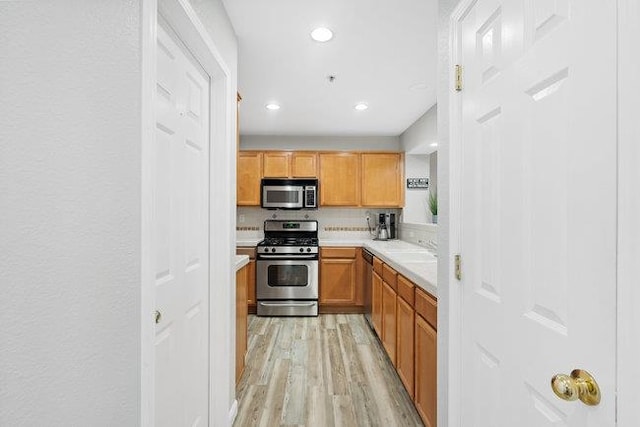 kitchen with tasteful backsplash, stainless steel appliances, sink, and light wood-type flooring