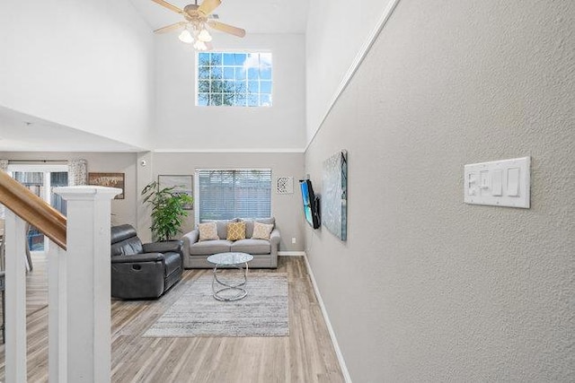 living room featuring light hardwood / wood-style flooring, ceiling fan, and a high ceiling