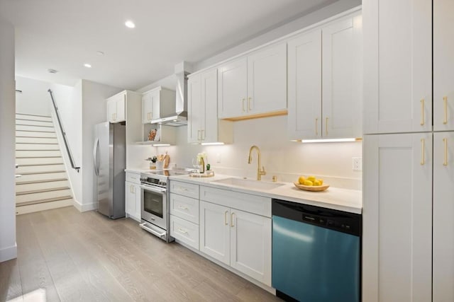 kitchen featuring appliances with stainless steel finishes, white cabinetry, sink, light wood-type flooring, and wall chimney exhaust hood