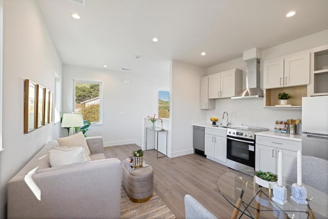 kitchen featuring wall chimney exhaust hood, sink, white cabinetry, light wood-type flooring, and stainless steel appliances