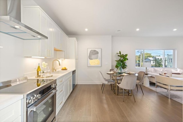 kitchen featuring wall chimney exhaust hood, sink, light hardwood / wood-style flooring, appliances with stainless steel finishes, and white cabinets