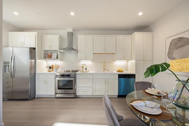 kitchen with sink, white cabinetry, stainless steel appliances, light hardwood / wood-style floors, and wall chimney exhaust hood