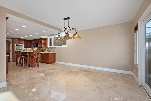 kitchen with a breakfast bar, a notable chandelier, pendant lighting, stainless steel appliances, and decorative backsplash