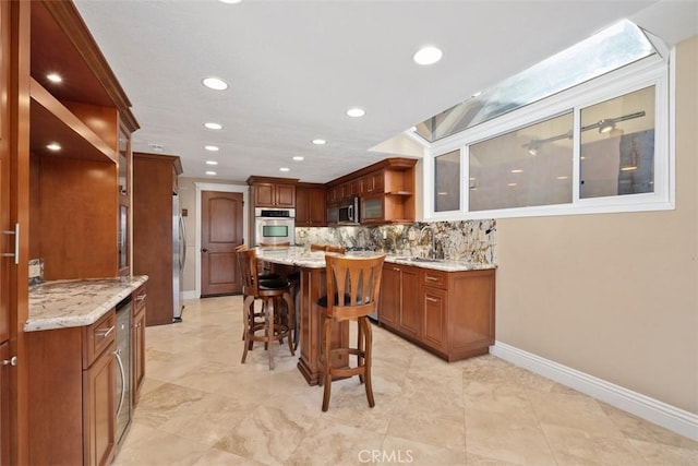 kitchen with a breakfast bar area, appliances with stainless steel finishes, light stone counters, a kitchen island, and decorative backsplash