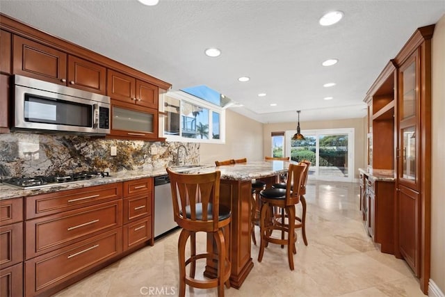 kitchen featuring a breakfast bar area, pendant lighting, stainless steel appliances, light stone countertops, and decorative backsplash