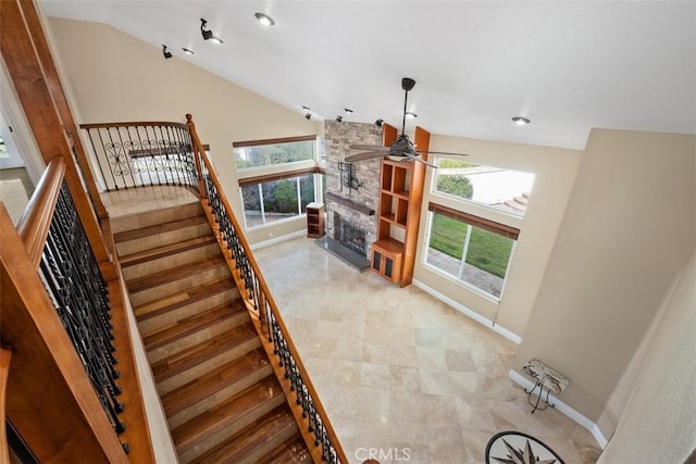 stairs with ceiling fan, a healthy amount of sunlight, a fireplace, and vaulted ceiling