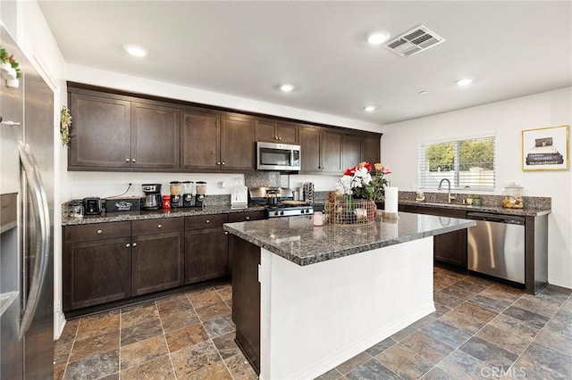 kitchen with dark brown cabinetry, sink, a center island, dark stone countertops, and stainless steel appliances