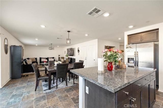 kitchen featuring a center island, hanging light fixtures, dark brown cabinets, dark stone countertops, and stainless steel fridge