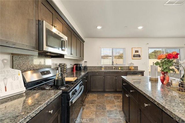 kitchen featuring dark brown cabinetry, sink, dark stone counters, and appliances with stainless steel finishes