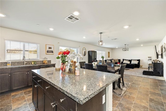 kitchen featuring sink, decorative light fixtures, a center island, dark brown cabinets, and light stone countertops