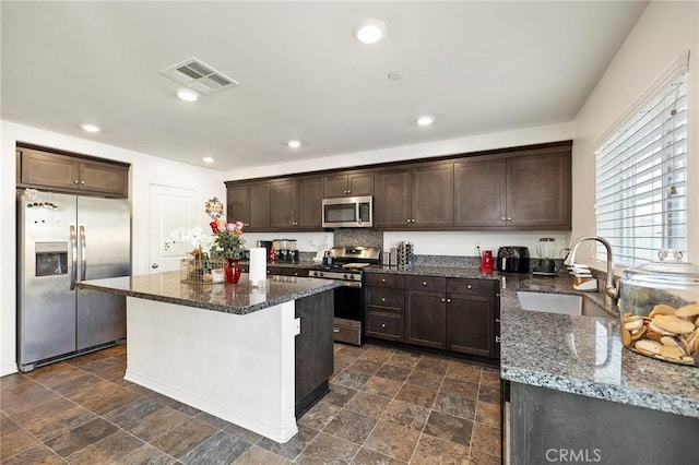 kitchen with sink, dark brown cabinets, dark stone counters, and appliances with stainless steel finishes