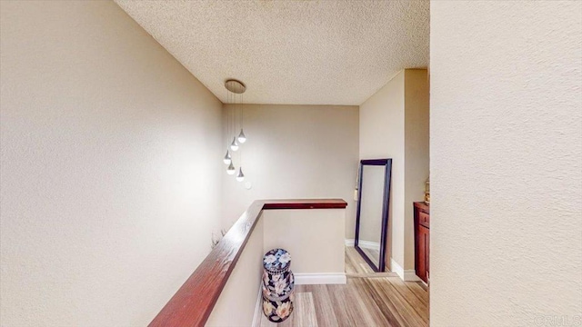 hallway with light wood-type flooring and a textured ceiling