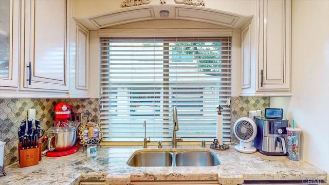 kitchen with tasteful backsplash, sink, cream cabinets, and light stone countertops