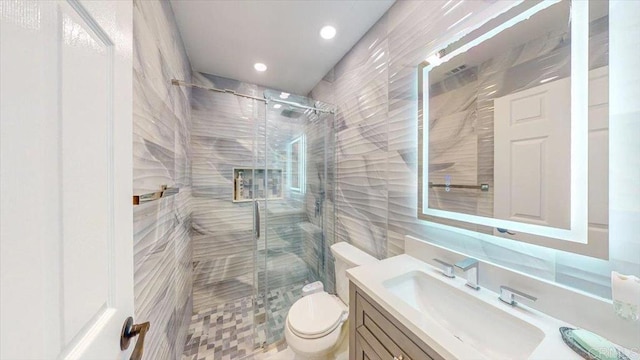 bathroom featuring vanity, toilet, a shower with shower door, and tile walls