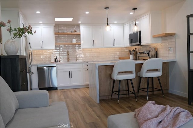 kitchen featuring appliances with stainless steel finishes, white cabinets, a kitchen breakfast bar, hanging light fixtures, and light hardwood / wood-style flooring