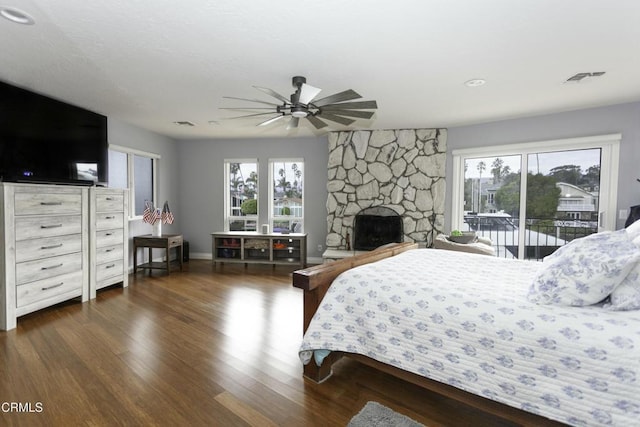 bedroom featuring multiple windows, dark hardwood / wood-style flooring, a stone fireplace, and access to outside