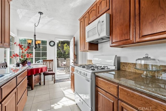 kitchen featuring pendant lighting, dark stone counters, light tile patterned floors, white appliances, and an inviting chandelier