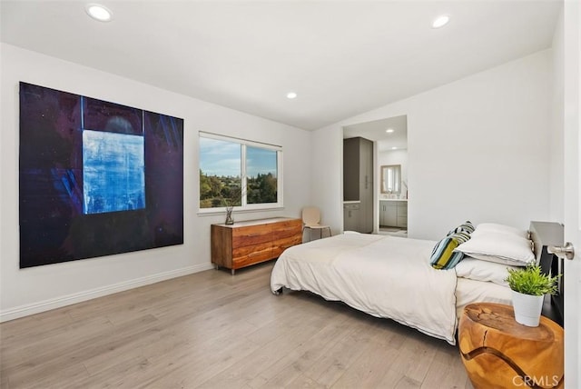 bedroom with lofted ceiling, connected bathroom, and light hardwood / wood-style flooring