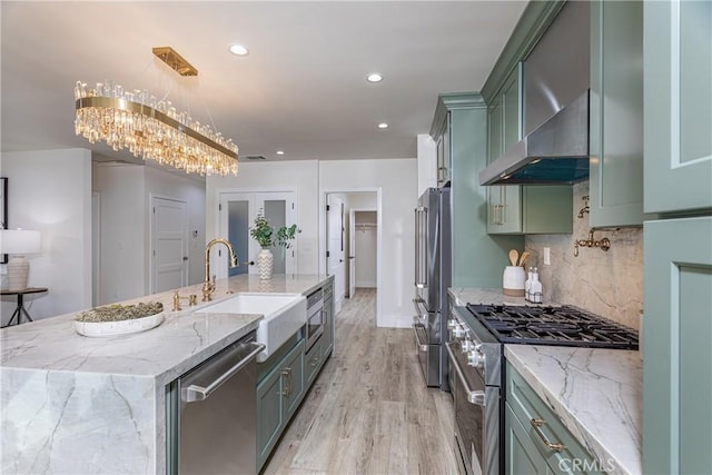 kitchen with sink, a large island, stainless steel appliances, light stone countertops, and wall chimney range hood