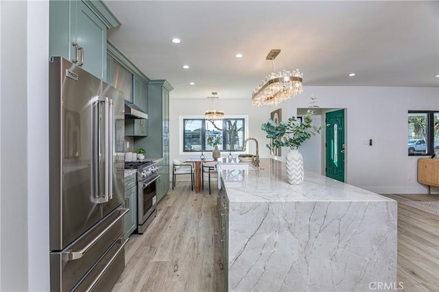 kitchen with a wealth of natural light, an island with sink, hanging light fixtures, high end appliances, and light stone countertops