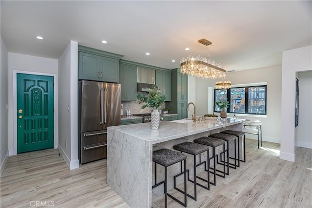 kitchen with pendant lighting, green cabinets, a kitchen island with sink, light stone countertops, and high quality fridge