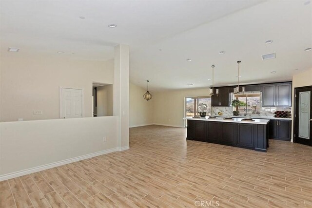 kitchen featuring vaulted ceiling, a kitchen island, decorative light fixtures, decorative backsplash, and light wood-type flooring