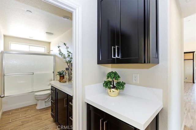 full bathroom featuring enclosed tub / shower combo, vanity, hardwood / wood-style floors, and toilet