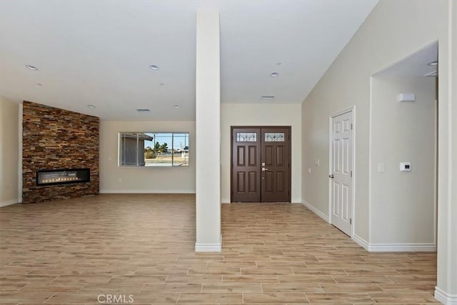 entryway featuring a stone fireplace, vaulted ceiling, and light hardwood / wood-style flooring