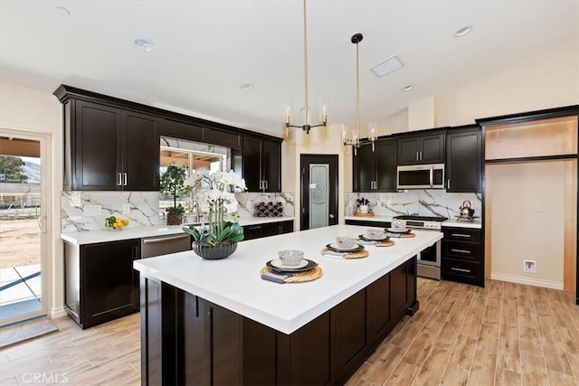 kitchen with a kitchen island, lofted ceiling, hanging light fixtures, stainless steel appliances, and light hardwood / wood-style flooring