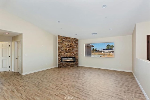 unfurnished living room with a stone fireplace, light hardwood / wood-style floors, and vaulted ceiling