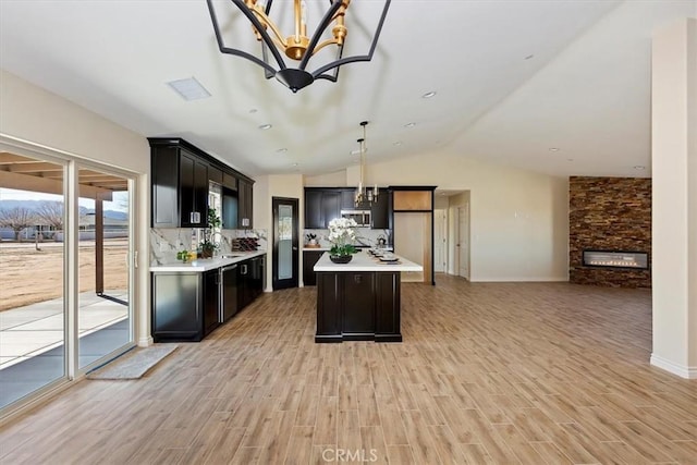 kitchen with a chandelier, hanging light fixtures, light wood-type flooring, a kitchen island, and a fireplace