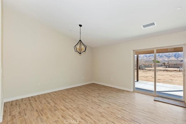 spare room featuring an inviting chandelier, a mountain view, and light wood-type flooring