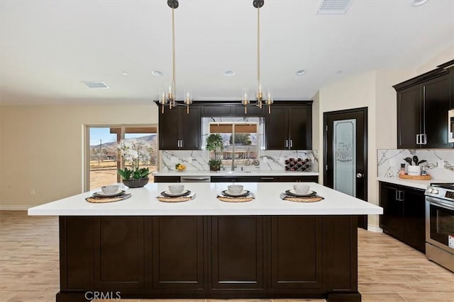 kitchen featuring hanging light fixtures, dark brown cabinets, a center island, tasteful backsplash, and stainless steel range oven