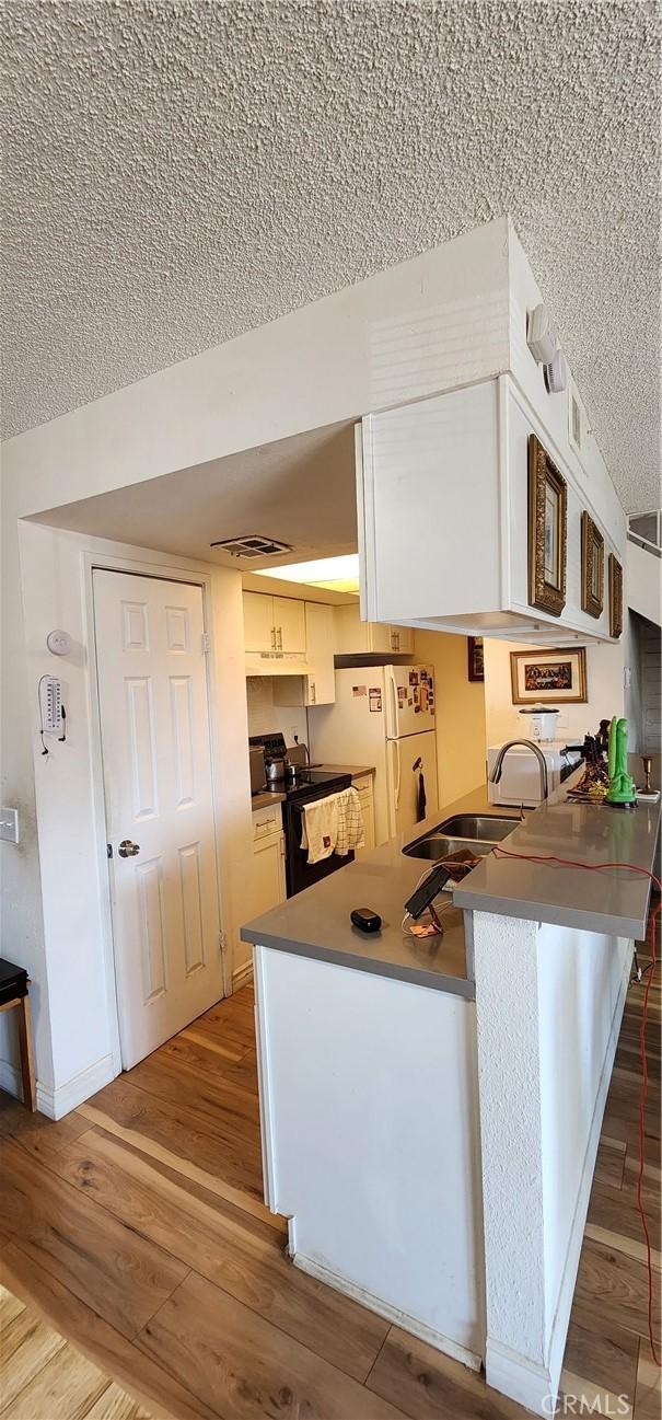 kitchen with black electric range oven, sink, white cabinetry, white refrigerator, and kitchen peninsula