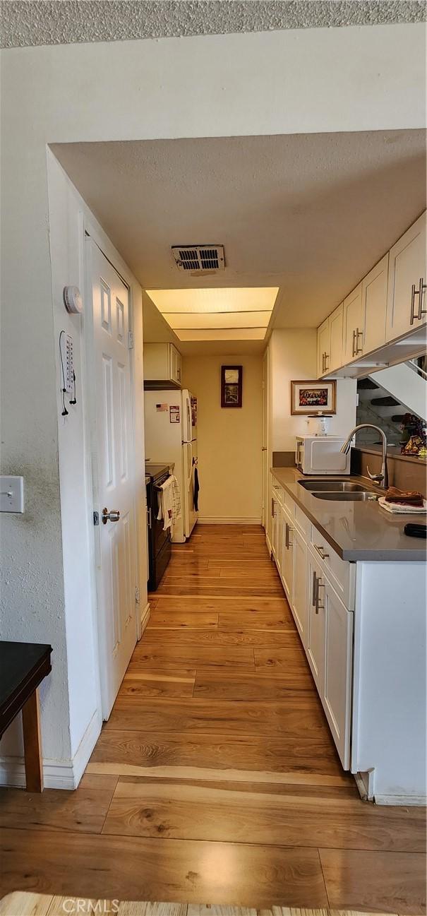 kitchen with white cabinetry, white appliances, sink, and light hardwood / wood-style flooring