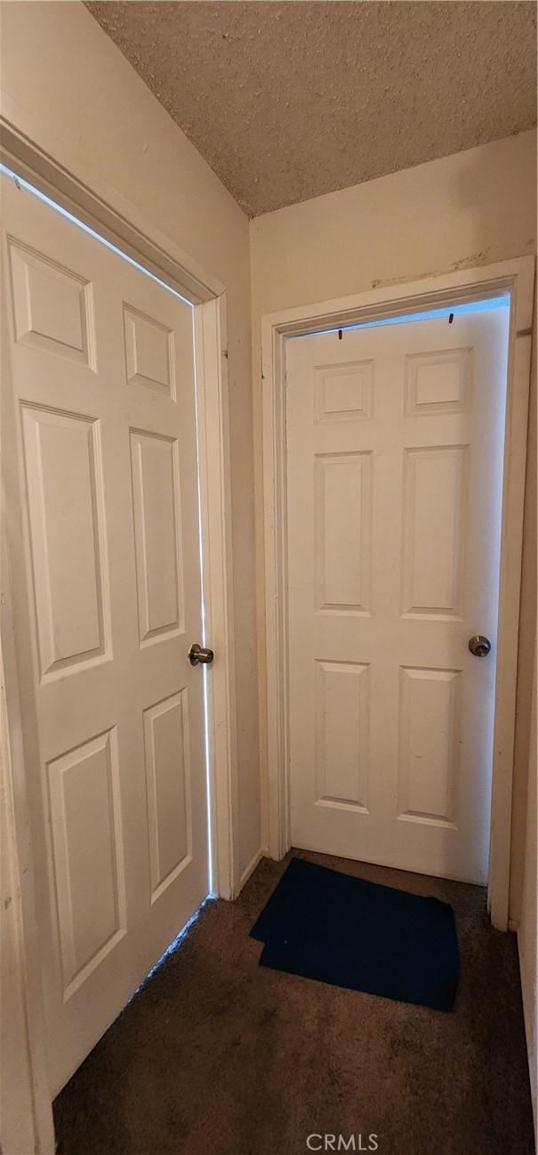 doorway to outside featuring a textured ceiling and dark carpet