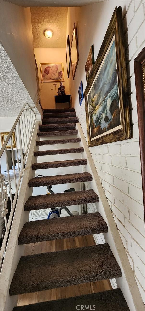 stairway with brick wall and a textured ceiling