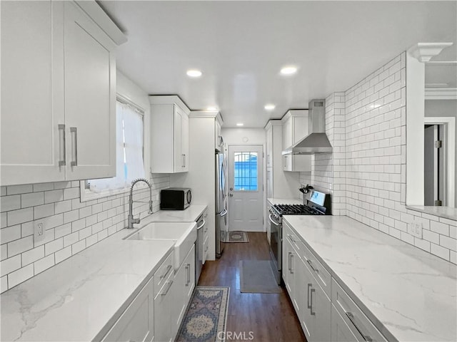 kitchen with appliances with stainless steel finishes, wall chimney range hood, white cabinets, and light stone counters