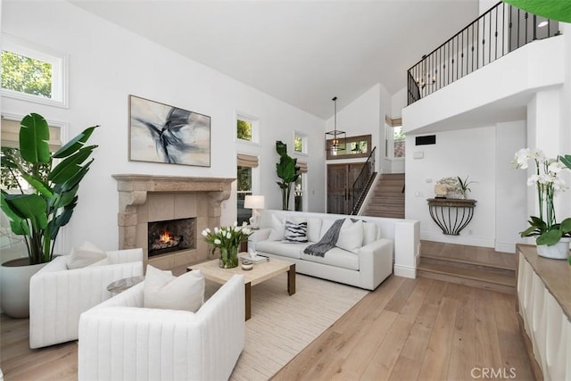 living room featuring light wood-type flooring, stairs, high vaulted ceiling, and a tile fireplace