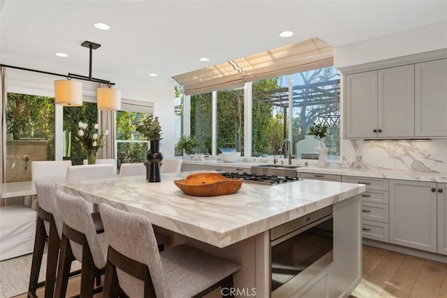 kitchen with light stone counters, light wood finished floors, appliances with stainless steel finishes, a kitchen breakfast bar, and tasteful backsplash