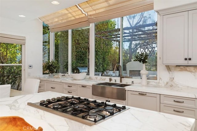 kitchen with recessed lighting, stainless steel gas stovetop, decorative backsplash, a sink, and light stone countertops