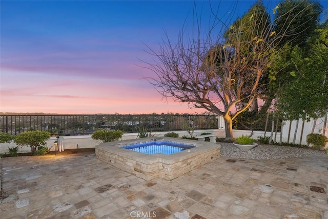 pool at dusk featuring fence, an in ground hot tub, and a patio area