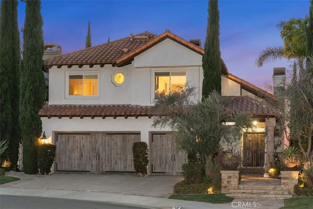 mediterranean / spanish house featuring an attached garage, a tile roof, concrete driveway, and stucco siding