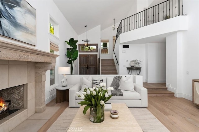 living room featuring high vaulted ceiling, baseboards, stairway, light wood finished floors, and a tiled fireplace