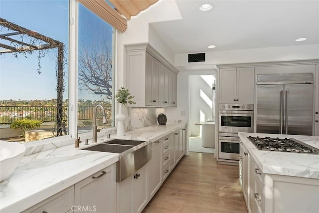 kitchen with light stone counters, light wood-style flooring, stainless steel appliances, a sink, and visible vents