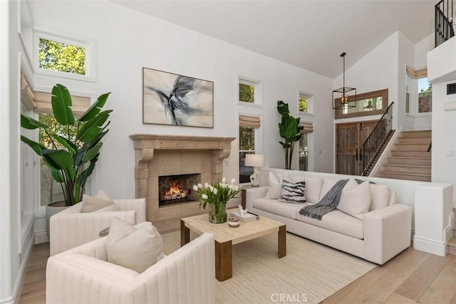 living area featuring high vaulted ceiling, stairway, a fireplace, and wood finished floors