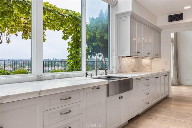 kitchen with tasteful backsplash, visible vents, light stone countertops, light wood-type flooring, and a sink