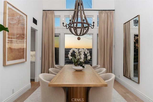 dining area with baseboards, visible vents, a towering ceiling, wood finished floors, and a chandelier