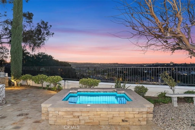 pool at dusk with a patio area, a swimming pool, and fence